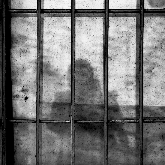 Sicht durch eine Gefängnistür hinter der sich der Schatten einer Frau abzeichnet, Bild in schwarz-weiß