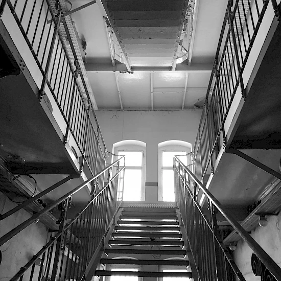 Blick nach oben eine Gefängnistreppe entlang in die höher gelegenen Flure, Bild in schwarz-weiß