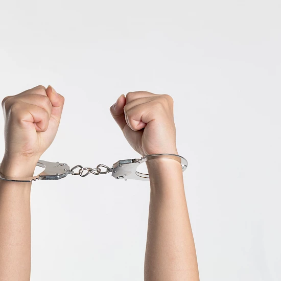 Nach oben gestreckte Arme einer Frau in Handschellen