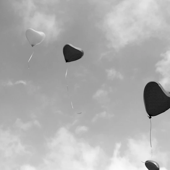 Verschiedenfarbige, herzförmige Luftballons fliegen gen Himmel. Bild in schwarz-weiß.
